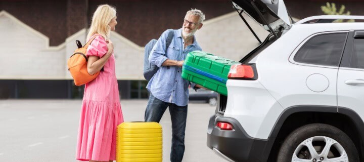 Happy couple loading their luggage to their car, preparing for road trip to Mexico. Long Term Mexico Insurance policy. 