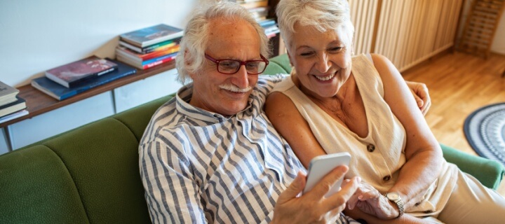 Smiling senior couple using WhatsApp on a smartphone together. Cheap Mexican Car Insurance.