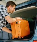 Man preparing for Mexico road trip, loading suitcase in car trunk. Cheap Mexican Insurance.