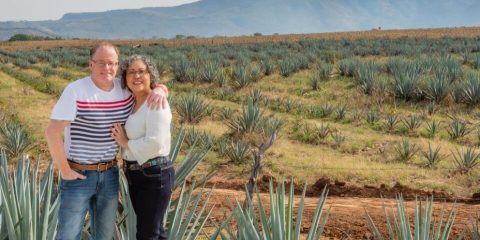 Retired couple in front of agave fields. Cheap Mexican auto insurance.