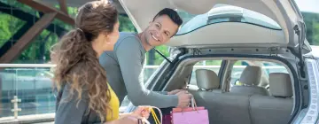 Pareja de turistas cargando compras en la cajuela de su auto con placas mexicanas antes de regresar de EE.UU.