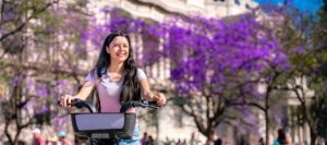 Woman riding a bike near Bellas Artes and jacarandas in Mexico City. Cheap Mexican Car Insurance.