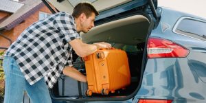 Man preparing for Mexico road trip, loading suitcase in car trunk. Cheap Mexican Insurance.